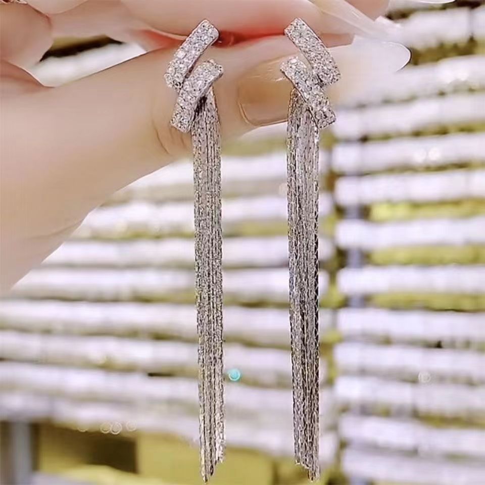 Silver tassel earrings held by a hand against