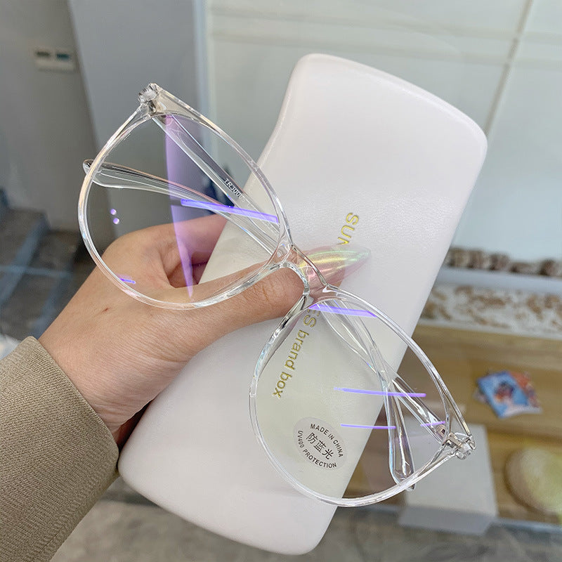Clear cat-eye glasses held by a hand with a white container in the background