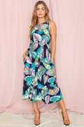 Woman wearing a sleeveless dress with a colorful leaf pattern against a pink background