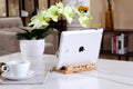 White tablet on a wooden stand with USB ports, next to a cup and saucer on a table.