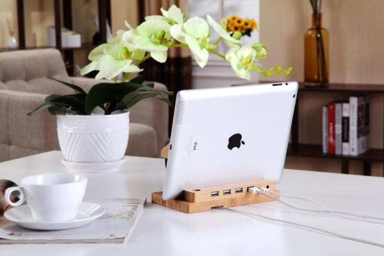 White tablet on a wooden stand with USB ports, next to a cup and saucer on a table.