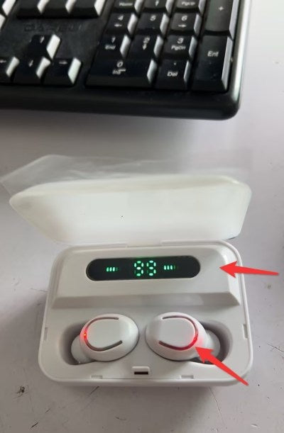 Wireless earbuds in a charging case with a digital display on a desk.