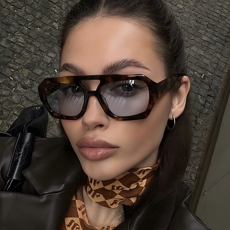 Woman wearing sunglasses with a patterned scarf around her neck, standing on a textured surface.