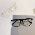 Black-framed eyeglasses on a white surface with a clear pair of sunglasses.