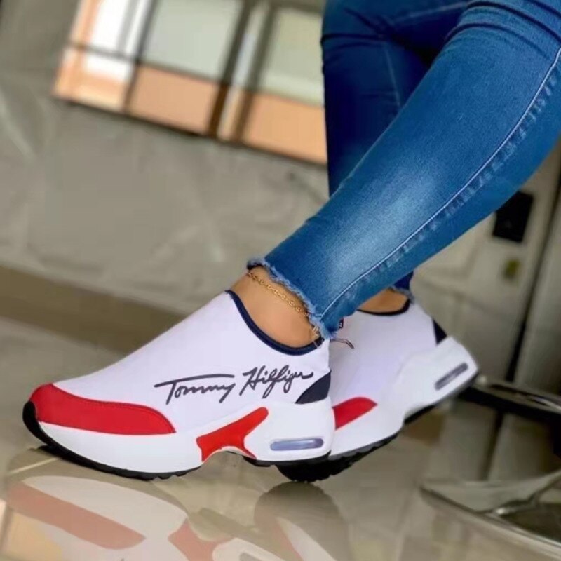 White sneakers with red and blue accents worn by a person sitting on a chair.