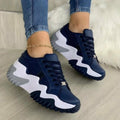Navy and white sneakers worn with blue jeans on a light wooden floor.