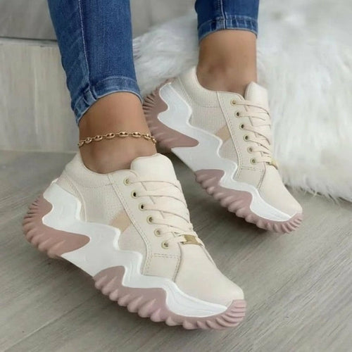 Beige and pink sneakers worn with blue jeans on a light wooden floor.
