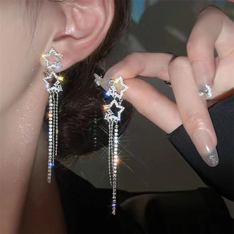 Star-shaped earrings with dangling elements worn by a person.