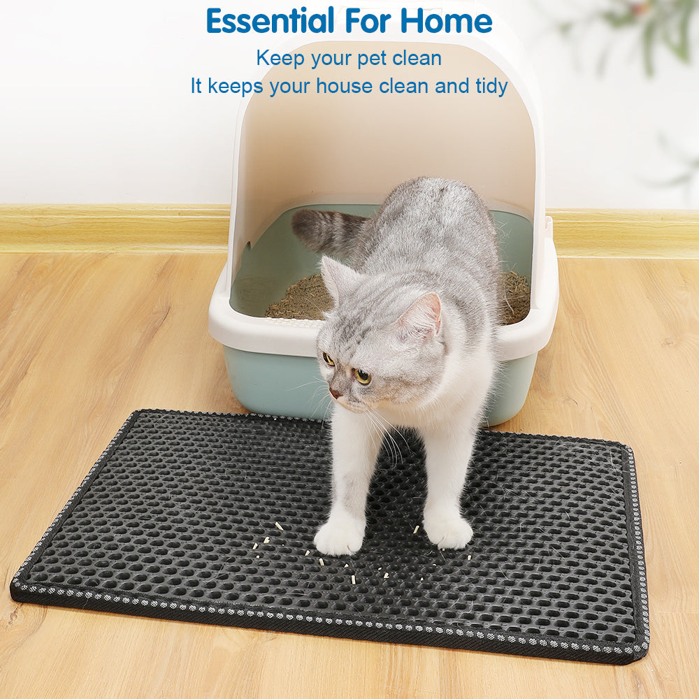 Cat using a black litter mat next to a litter box on a wooden floor.