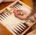 Hand holding dice over a backgammon board with pieces and a box.
