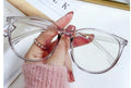 Clear cat-eye glasses held by a hand with pink nail polish 