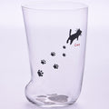 Clear glass tumbler with black paw prints and a cat illustration on a light purple background