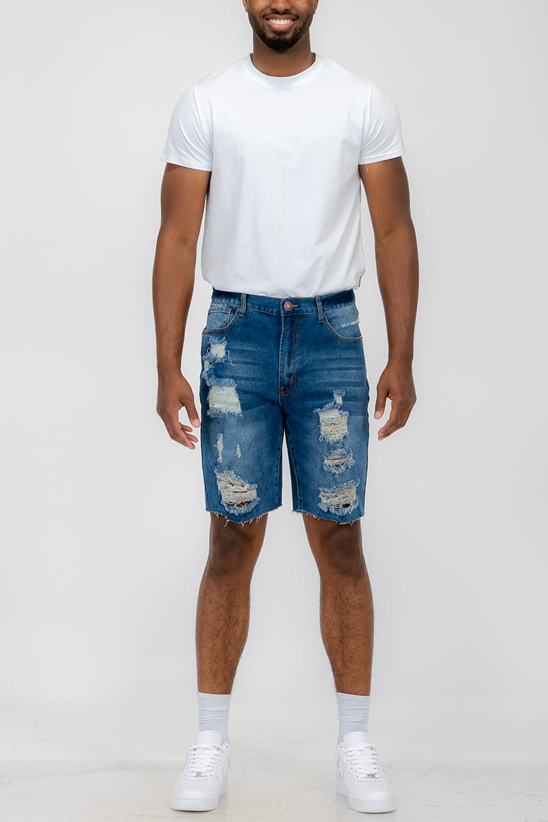 Man wearing a white t-shirt and blue distressed denim shorts on a plain background