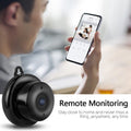 Person holding a smartphone with a security camera app on screen, next to a small black security camera.
