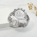 Silver watch with engraved text on a white surface with dried flowers
