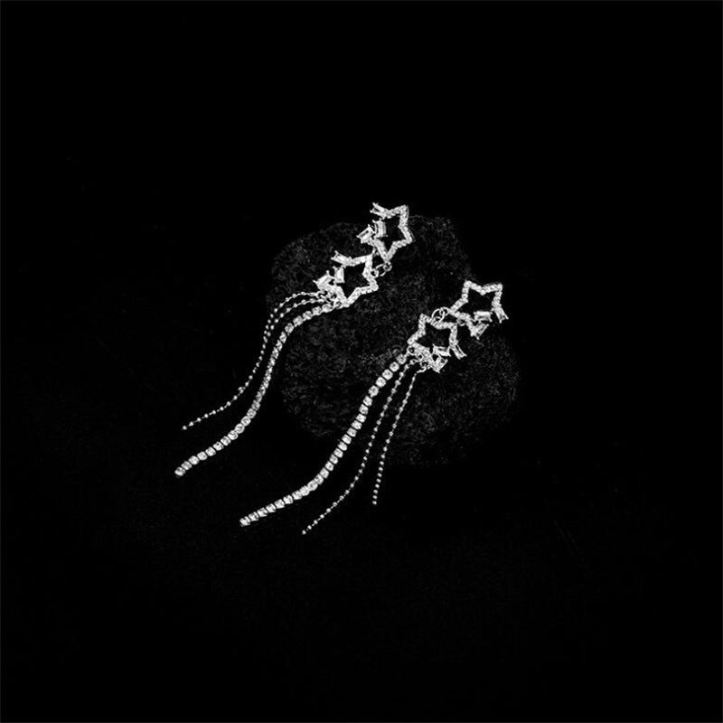 Star-shaped earrings with dangling elements worn by a person.